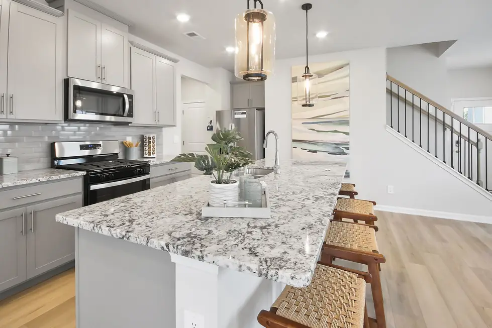 Kitchen island in granite and white cabinetry under pendant lighting, photographed for a listing