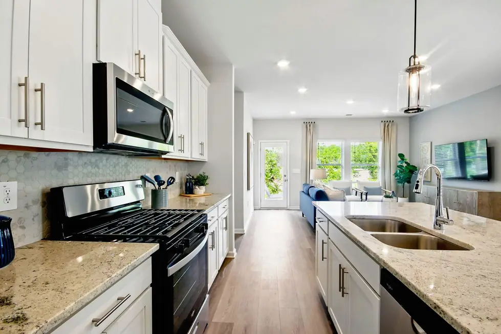 Galley kitchen in white cabinetry with stainless appliances and a hexagon tile backsplash, looking through to the living room
