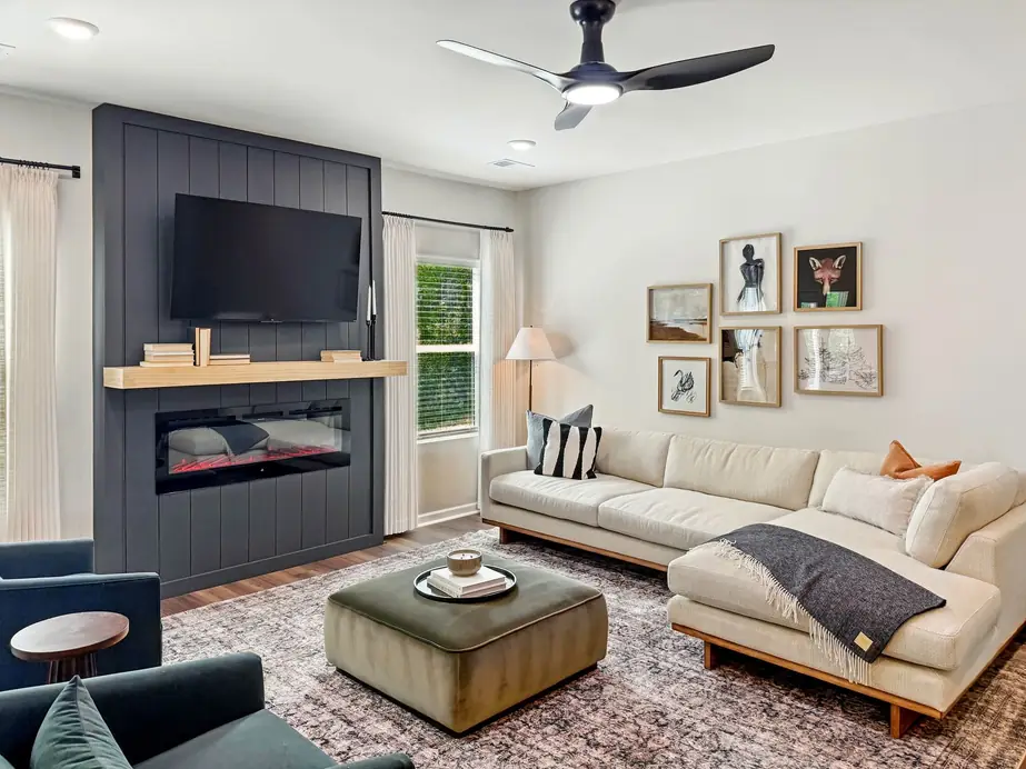 Living room with a built-in dark panel fireplace wall, cream sectional and a gallery wall of framed prints, photographed for a listing